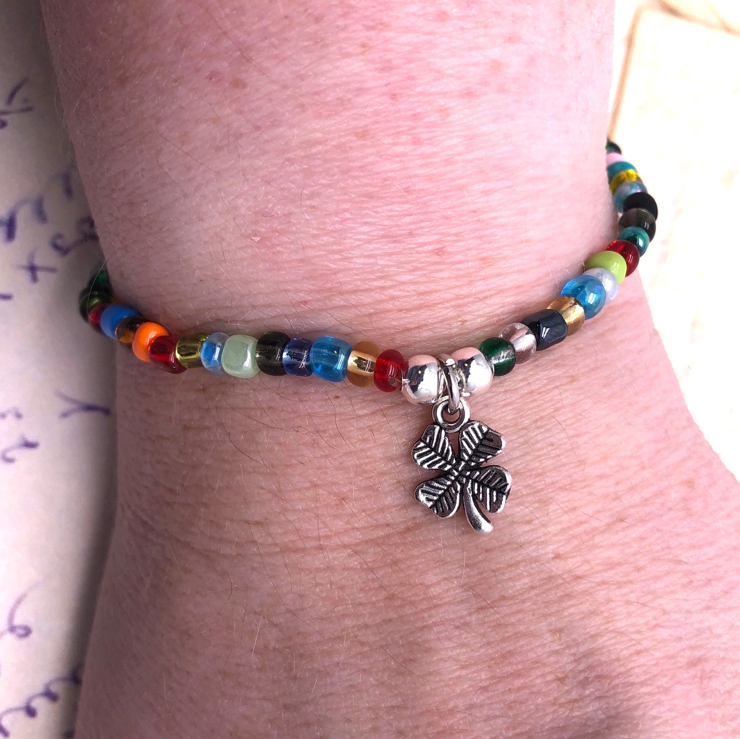 A colorful beaded bracelet with a silver clover charm on a person's wrist.