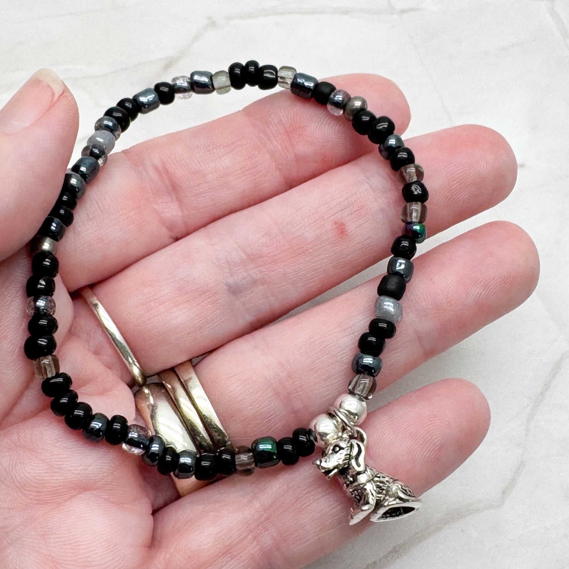 A hand holding a bracelet made of black beads and silver beads, with a charm attached to it.