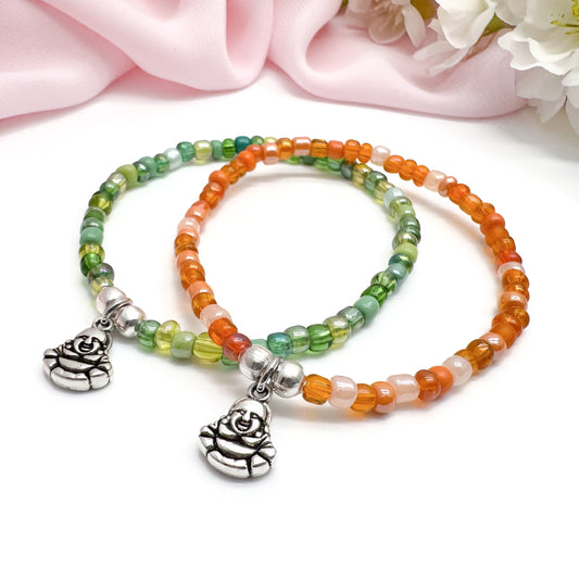Two colorful beaded bracelets with charms, placed on a white surface with a pink fabric background.