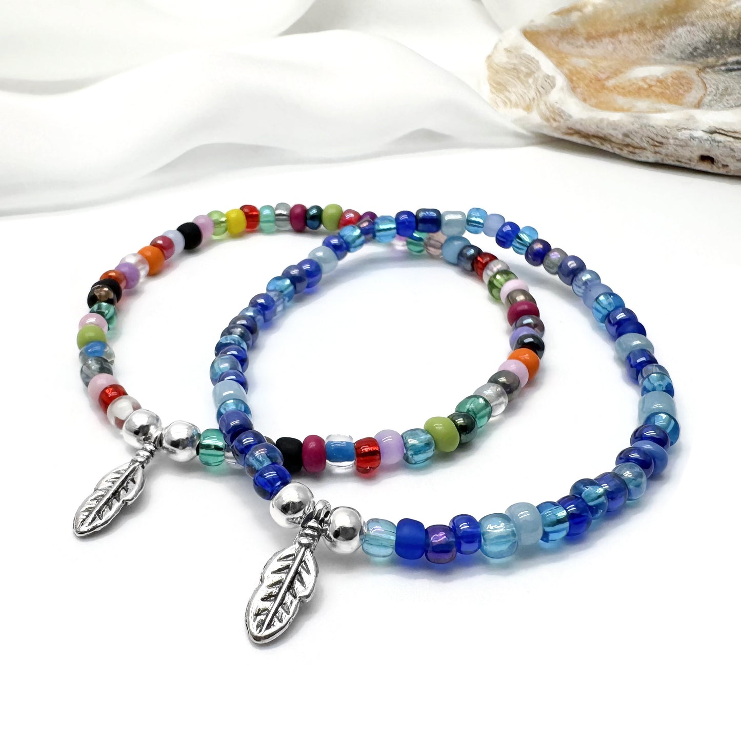 two colorful beaded bracelets with metal leaf charms, placed on a white surface.