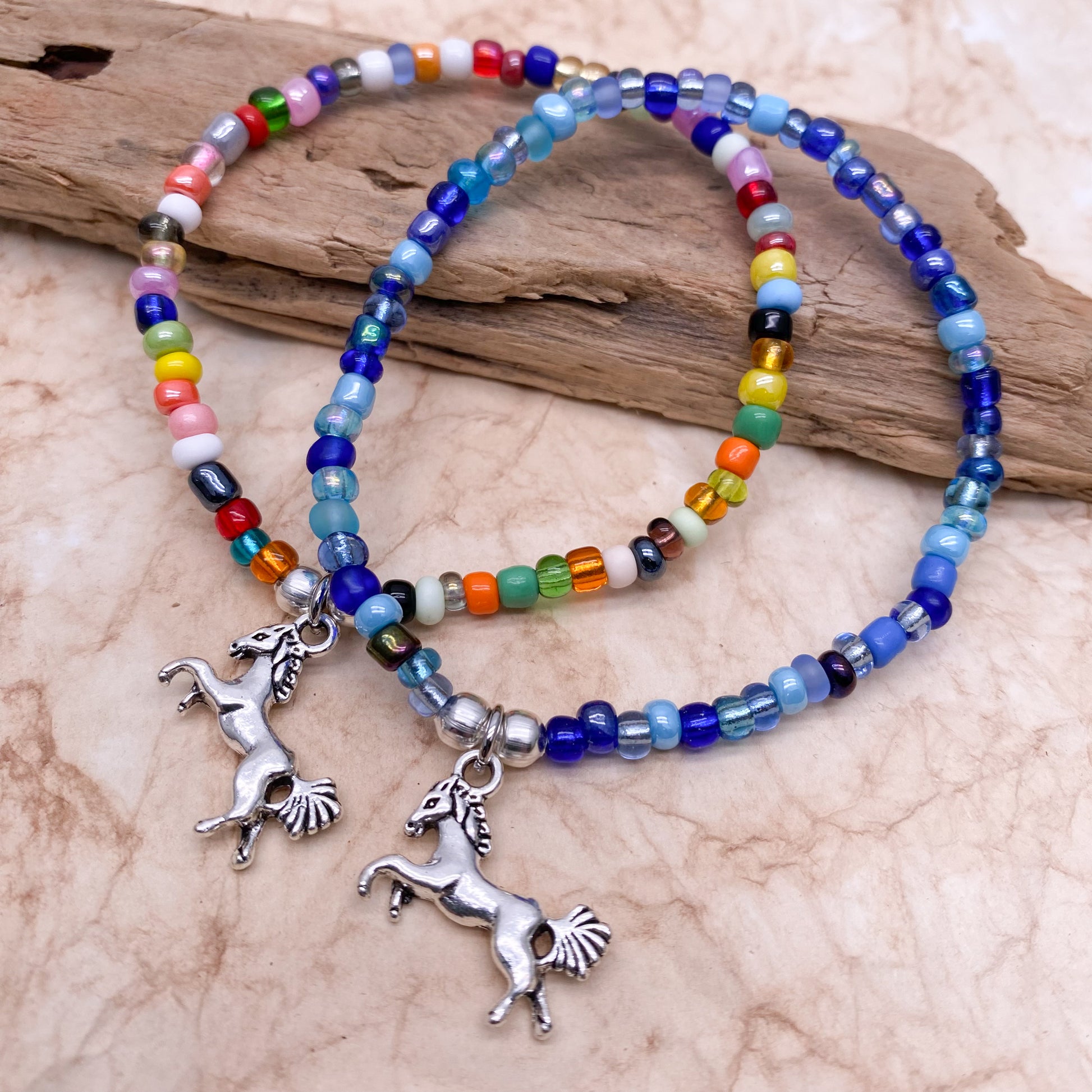 Two beaded bracelets with charms in the shape of horses are displayed on a wooden surface.