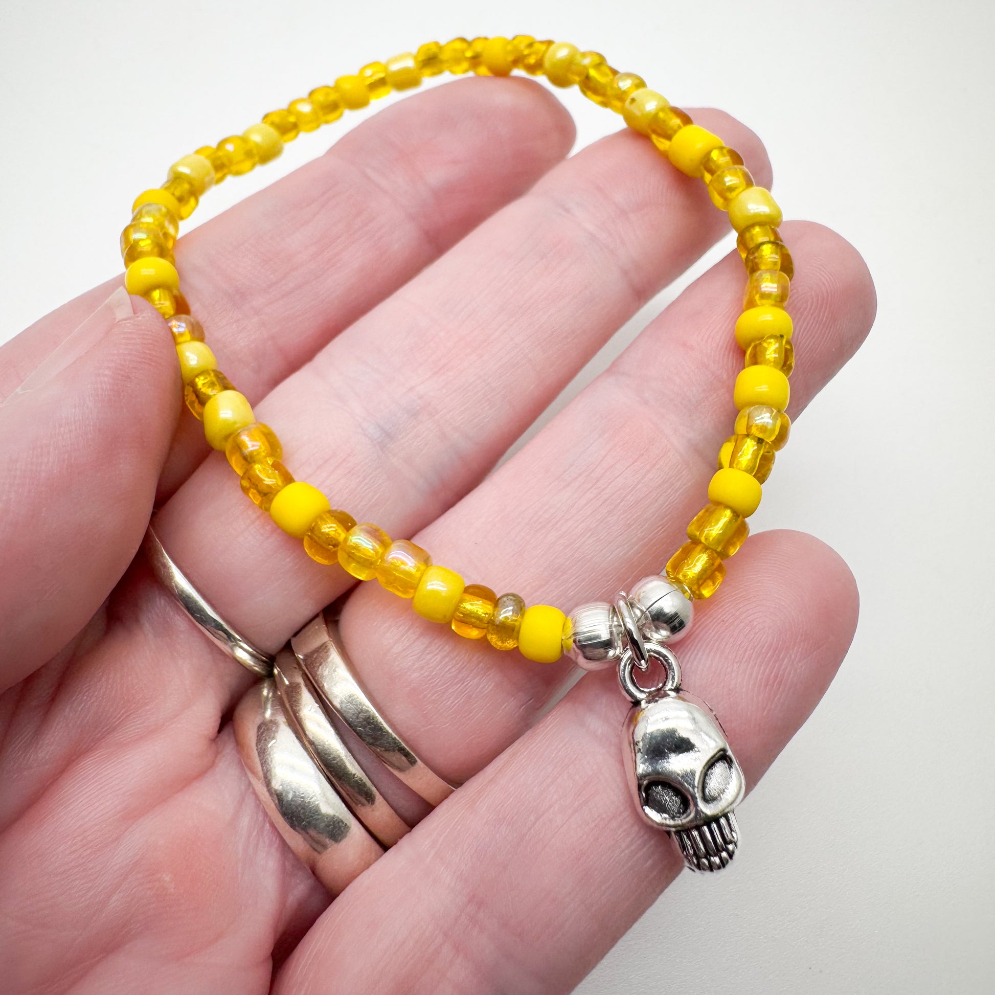 A hand holding a yellow bead bracelet with a silver skull charm.