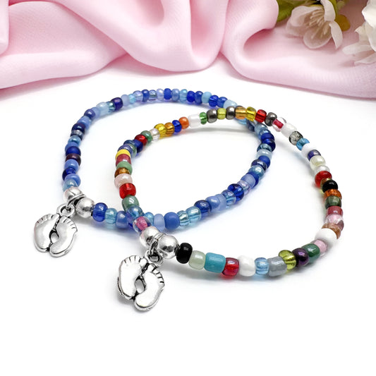 Two colorful beaded bracelets with metal charms, one silver and one silver with a foot charm, are displayed on a white surface.