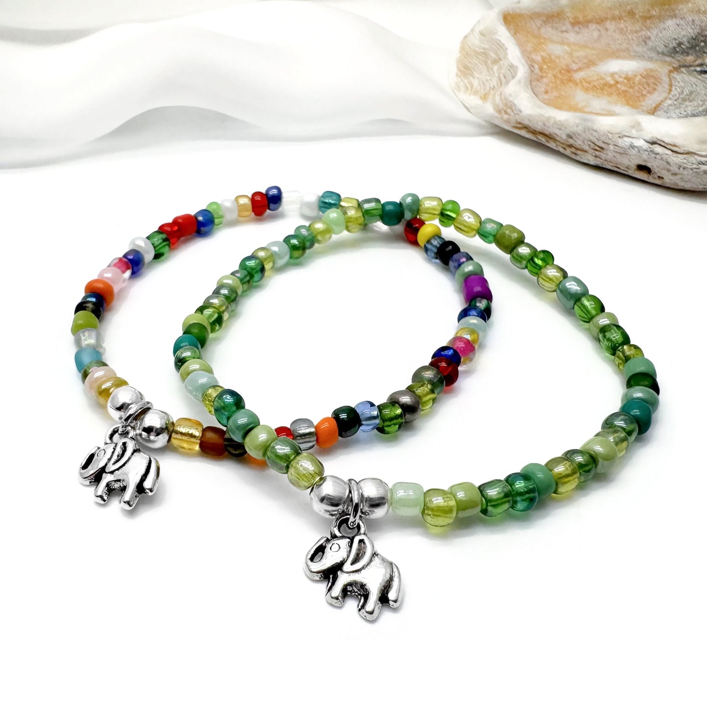two colorful beaded bracelets with elephant charms, placed on a white surface.