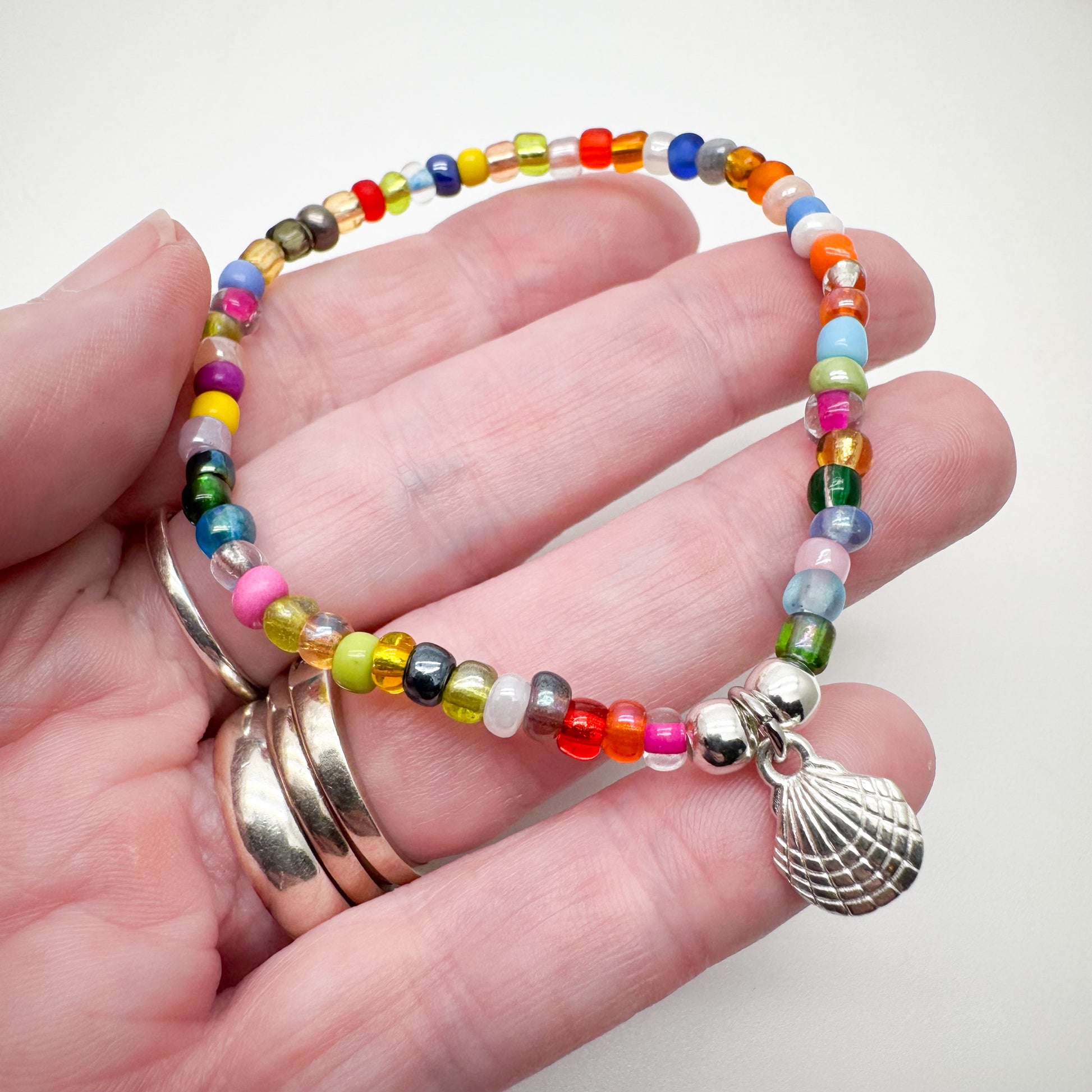 A hand holding a colorful beaded bracelet with a seashell charm.