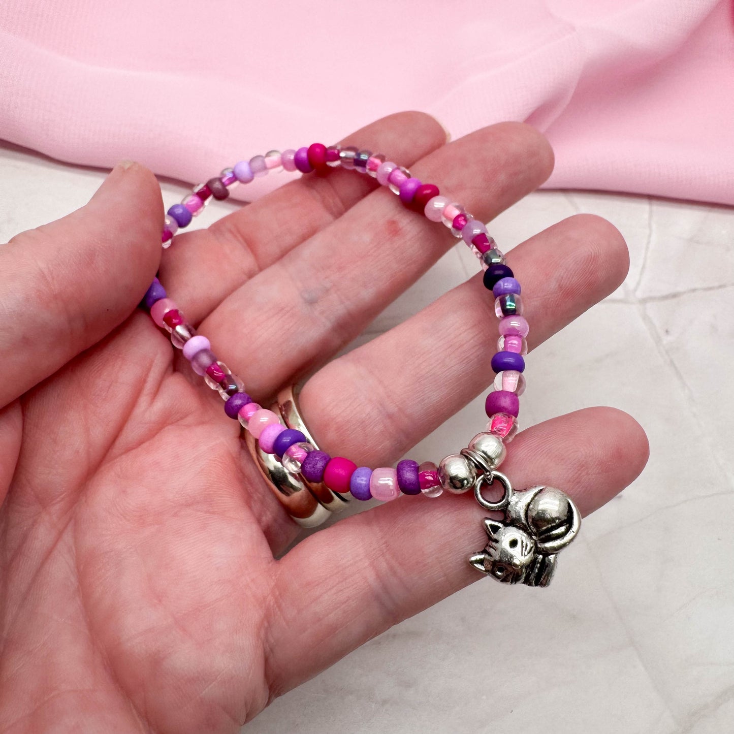 A hand holding a bracelet made of colorful beads, with a charm featuring a cat design.