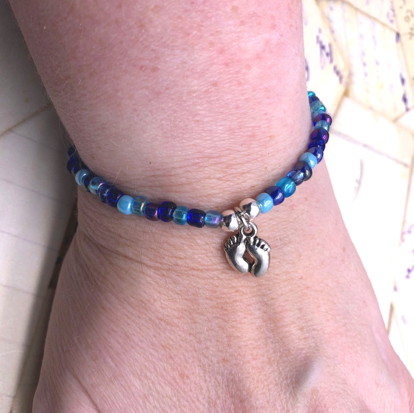 A bracelet made of blue beads and silver charms, with a charm featuring a pair of feet.