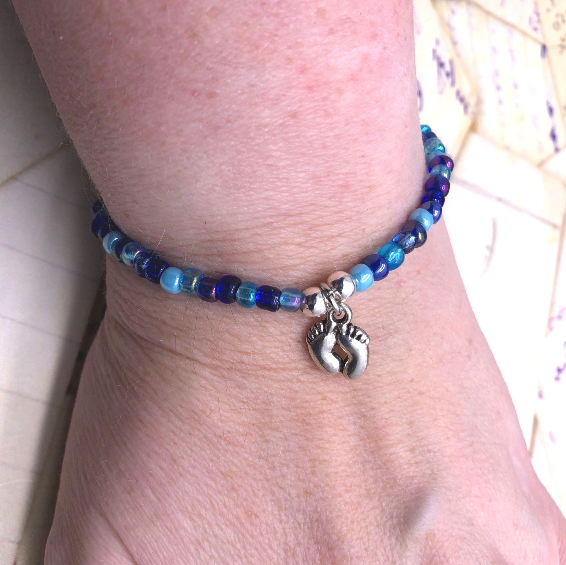 A bracelet made of blue beads and silver charms, with a charm featuring a pair of feet.