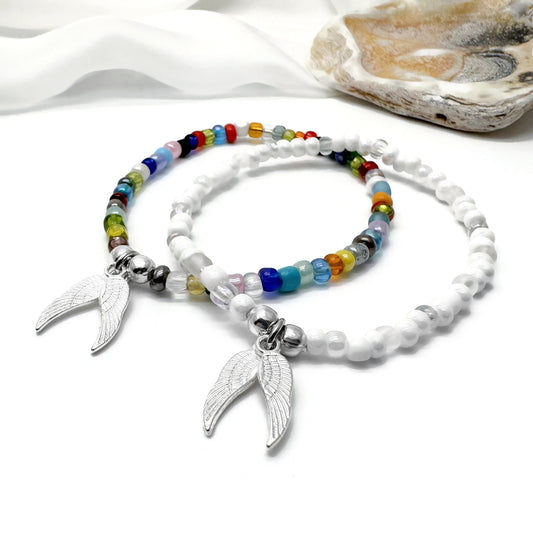 two beaded bracelets with silver wing charms, placed on a white surface.