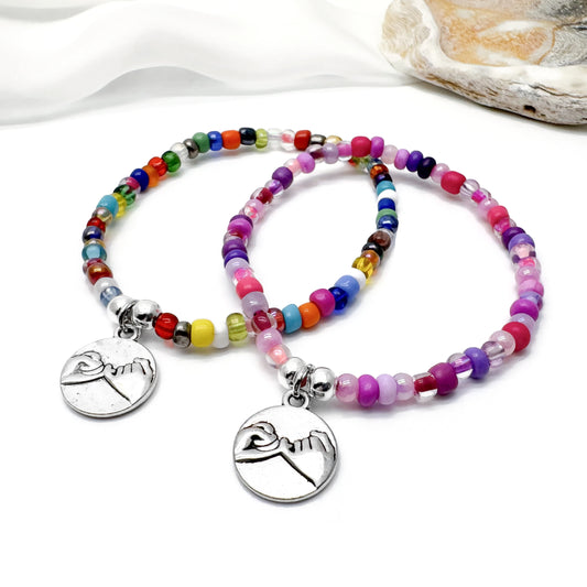 Two beaded bracelets with charms on them, placed on a white surface.