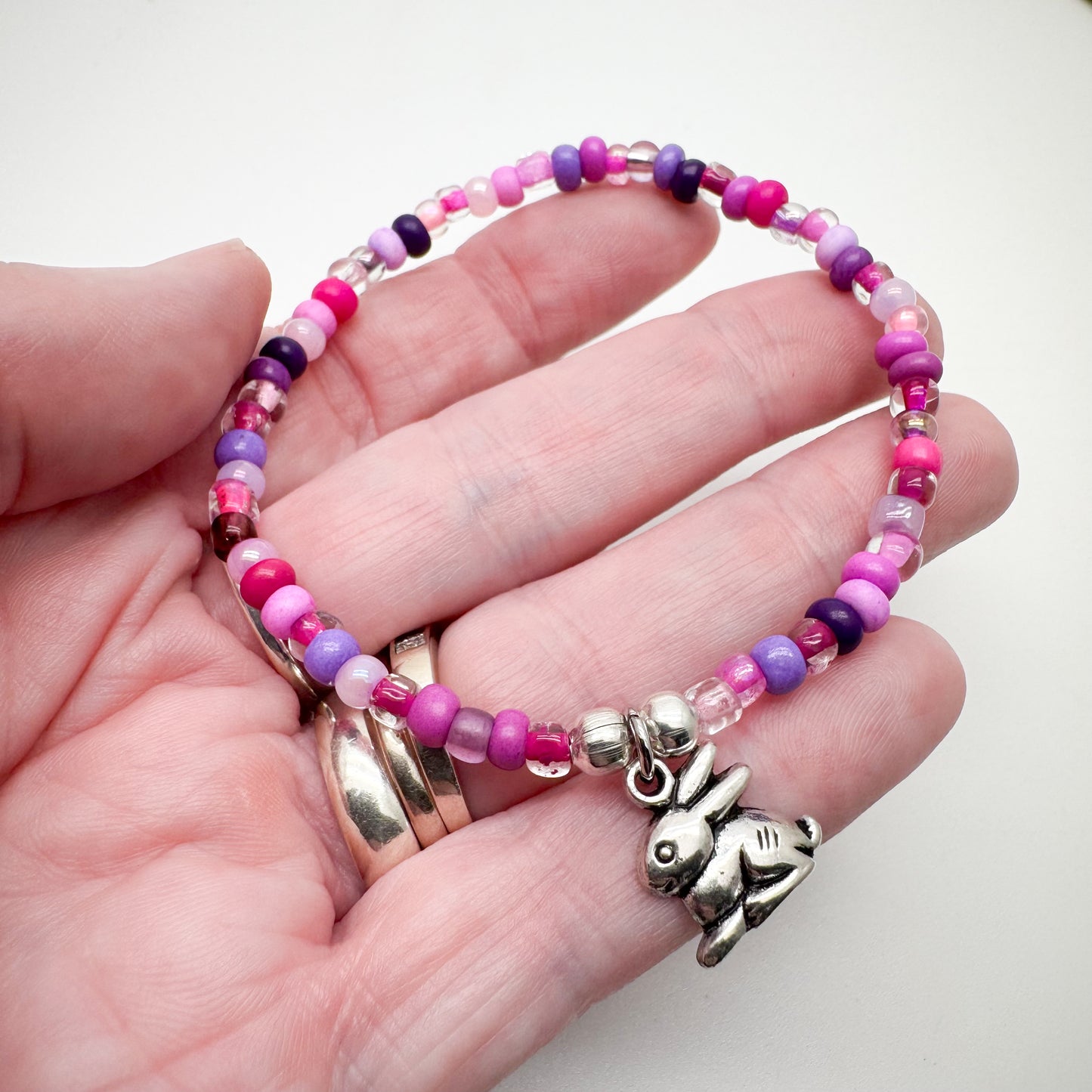 A hand holding a bracelet made of colorful beads and a charm featuring a rabbit.