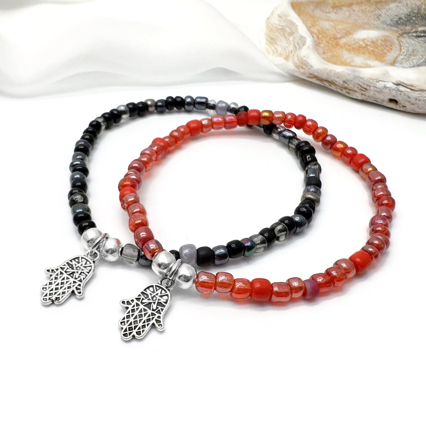 two beaded bracelets with metal charms, one with a black and red color scheme and the other with a red and black color scheme.