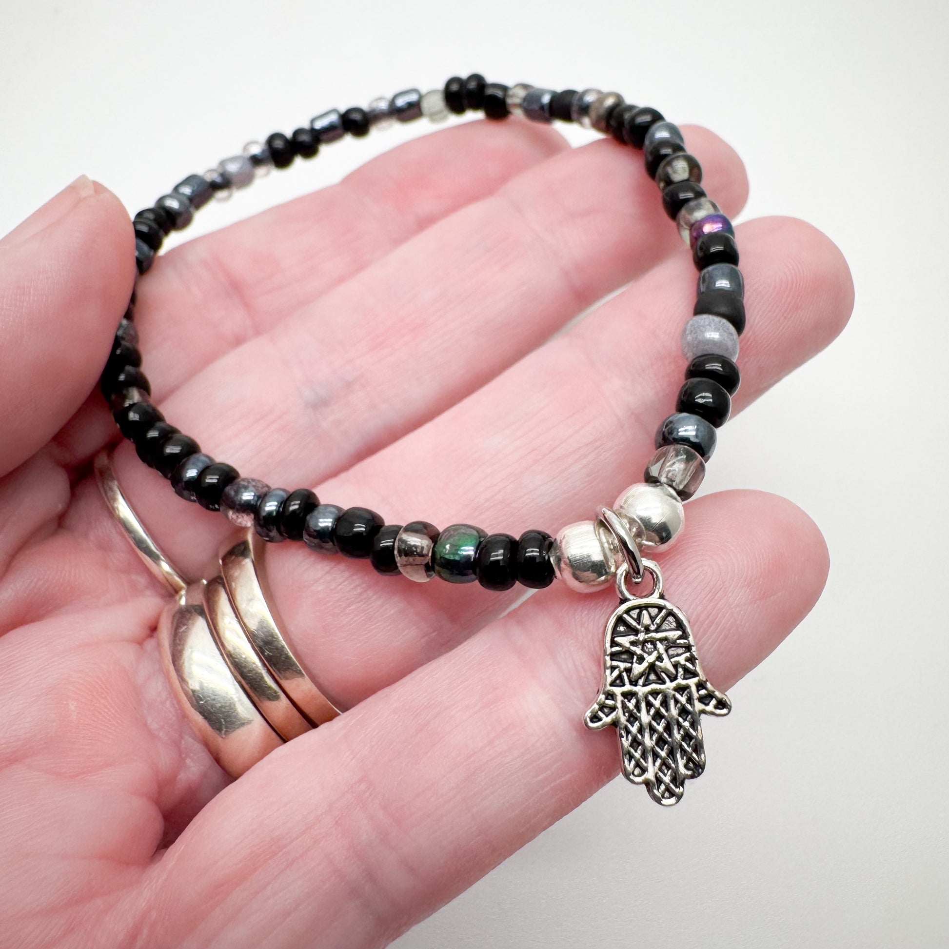 A hand holding a bracelet with black beads and a silver charm featuring a hand design.