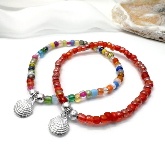 two colorful beaded bracelets with metal charms, including shells, arranged on a white surface.