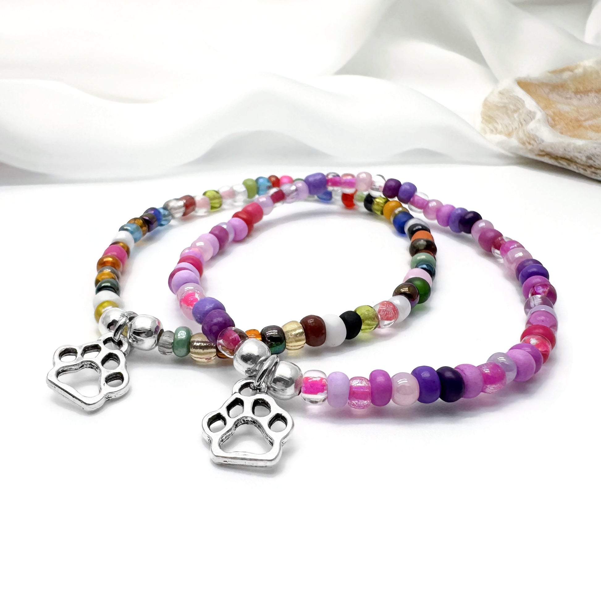 Two colorful beaded bracelets with silver paw print charms are displayed on a white surface.