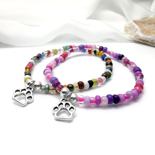 Two colorful beaded bracelets with silver paw print charms are displayed on a white surface.