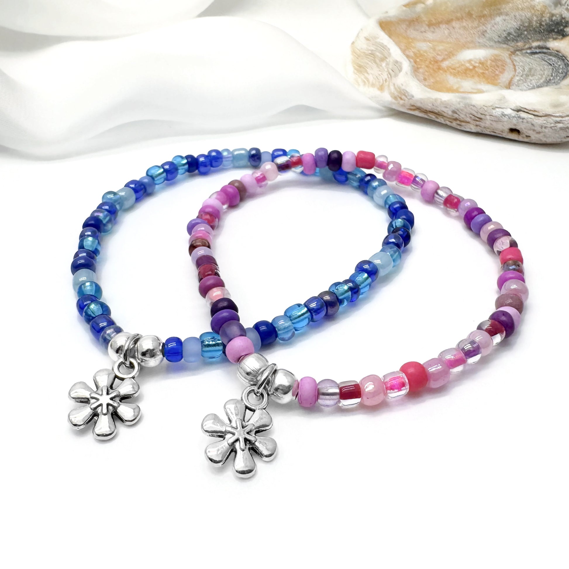 two colorful beaded bracelets with flower charms, placed on a white surface.