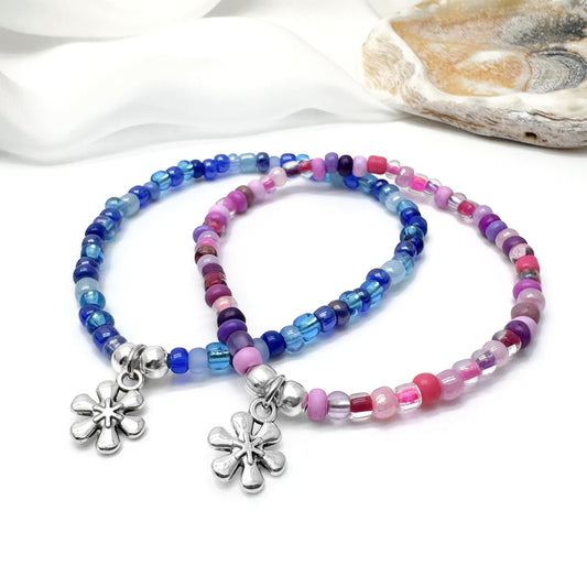 two colorful beaded bracelets with flower charms, placed on a white surface.