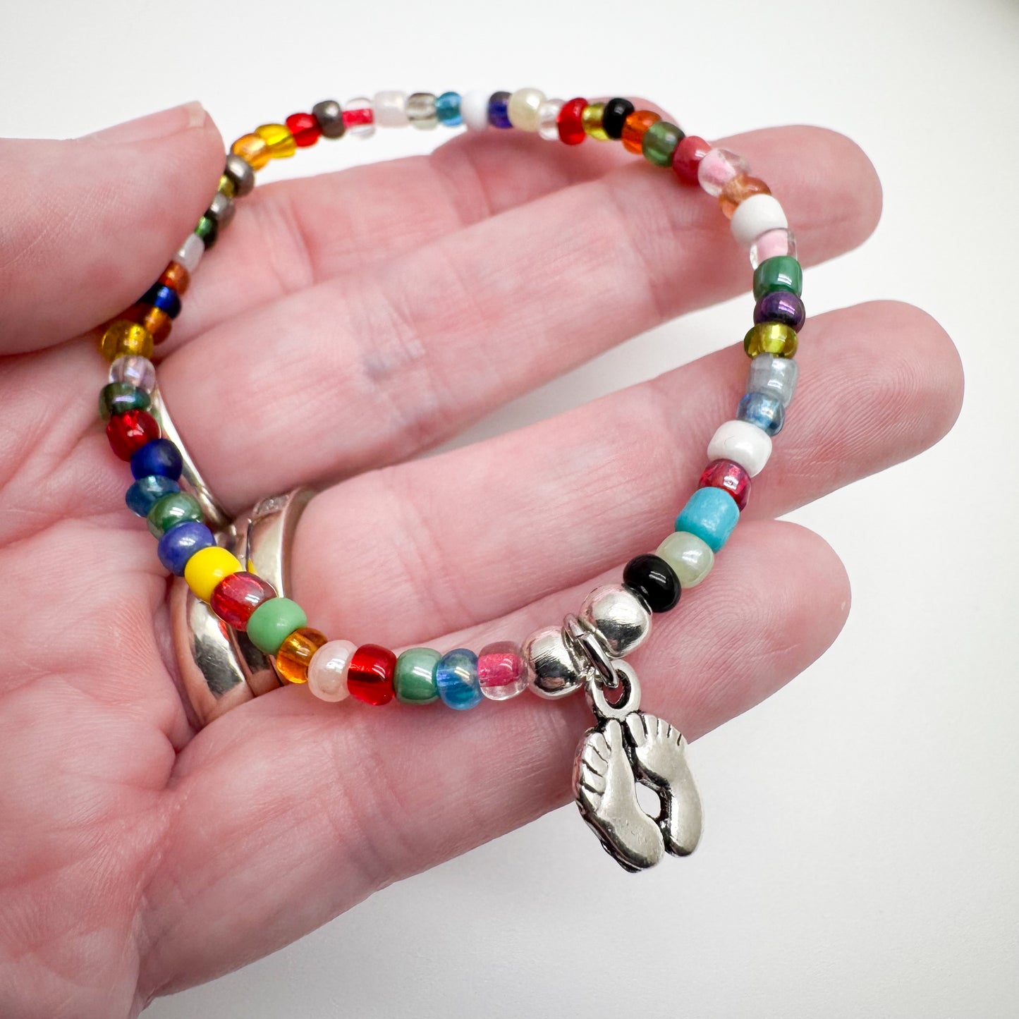 A hand holding a colorful beaded bracelet with a charm featuring a pair of feet.