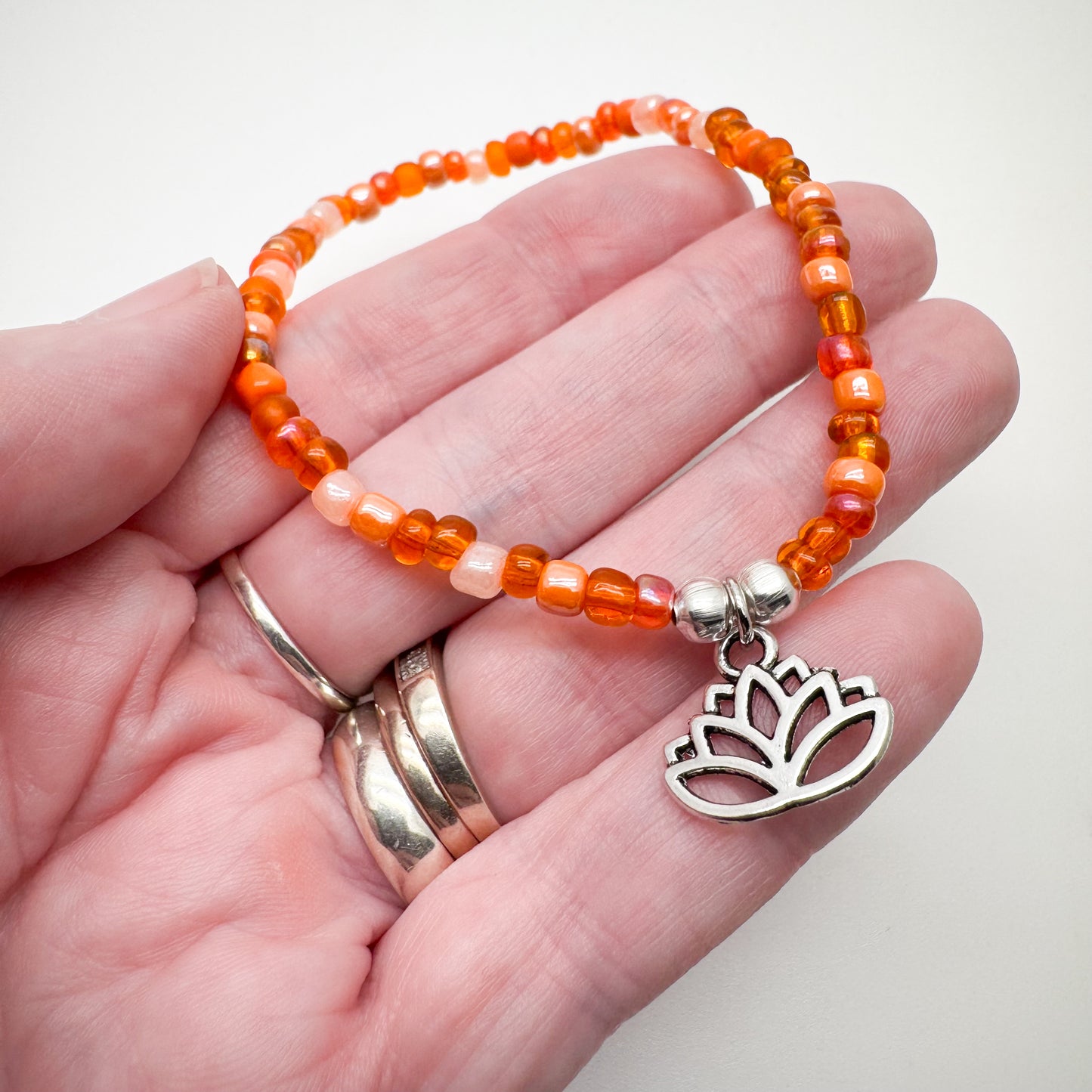 A hand holding a bracelet made of orange beads and a silver lotus flower charm.