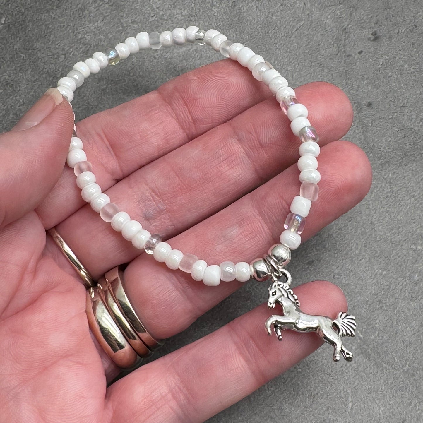 A hand holding a bracelet with white beads and a silver charm in the shape of a horse.