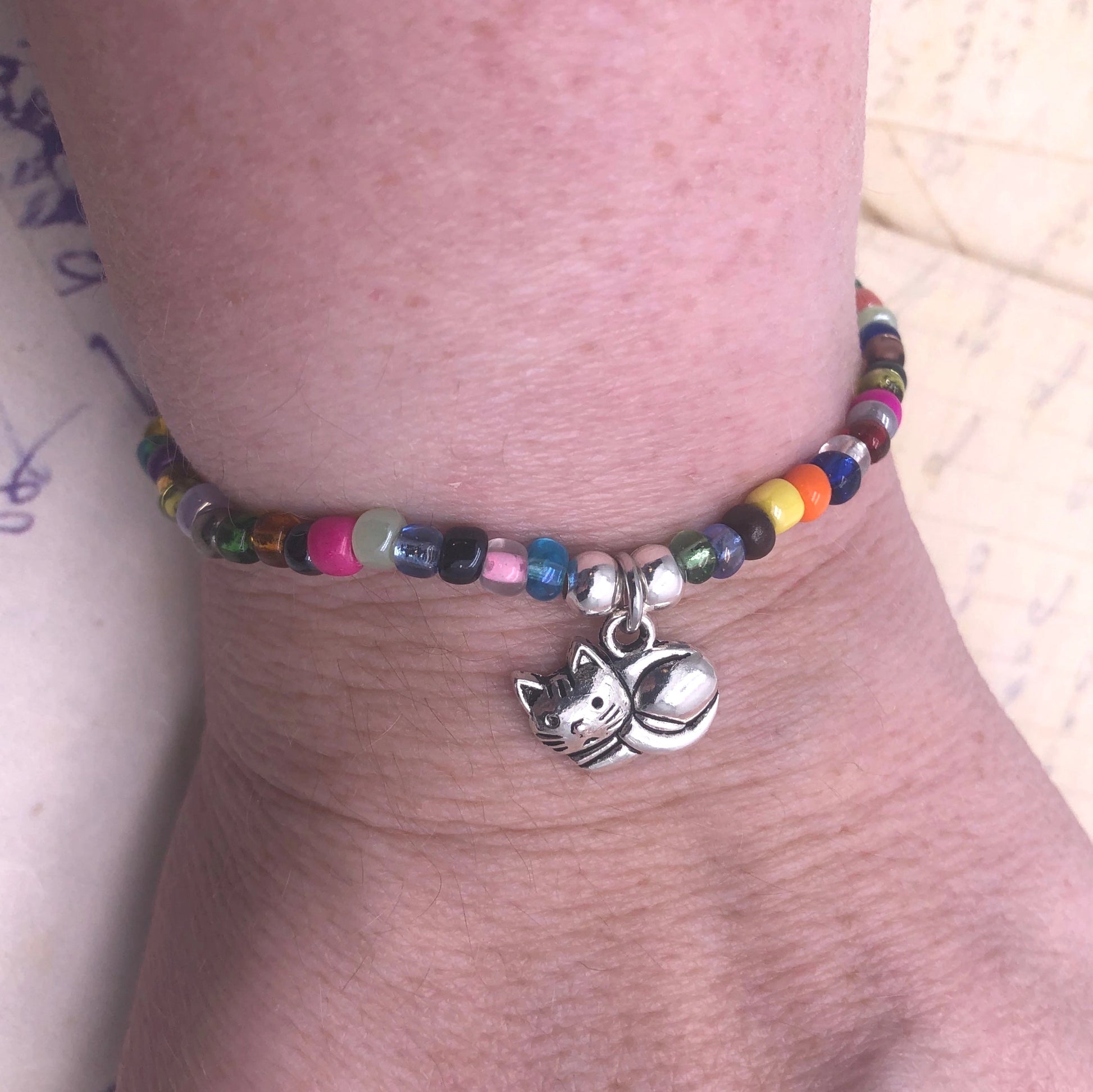 A colorful beaded bracelet with a charm featuring a cat is worn on a person's wrist.