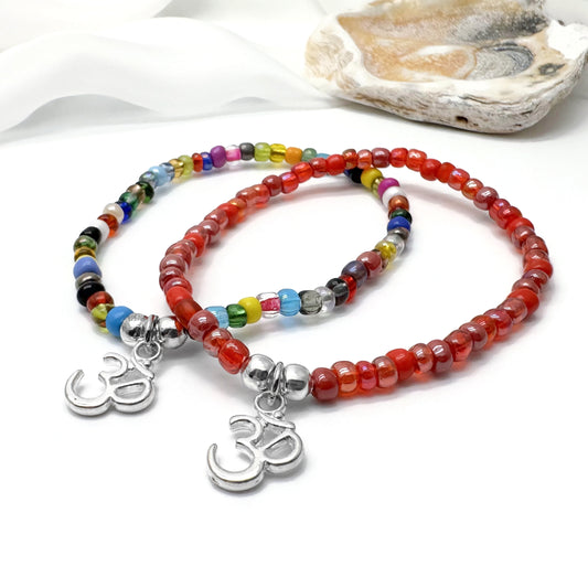 two beaded bracelets with charms, one red and one blue, placed on a white surface.