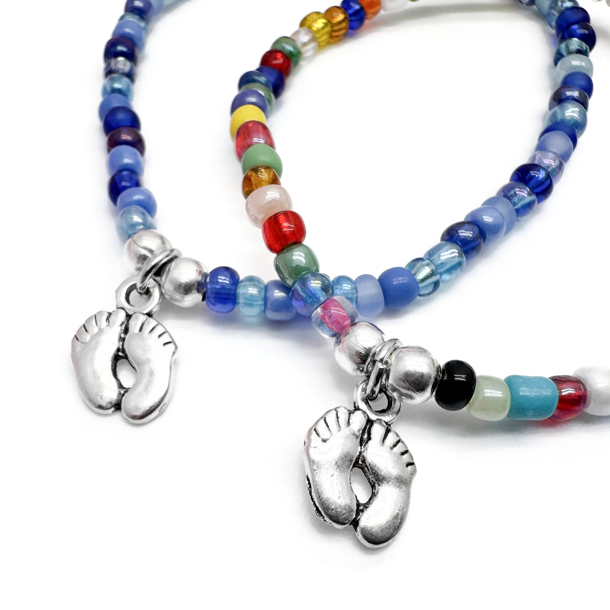 two beaded bracelets with metal charms, one of which is a pair of feet.