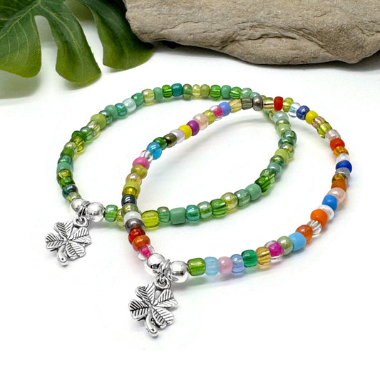 two colorful beaded bracelets with clover charms, placed on a white surface.