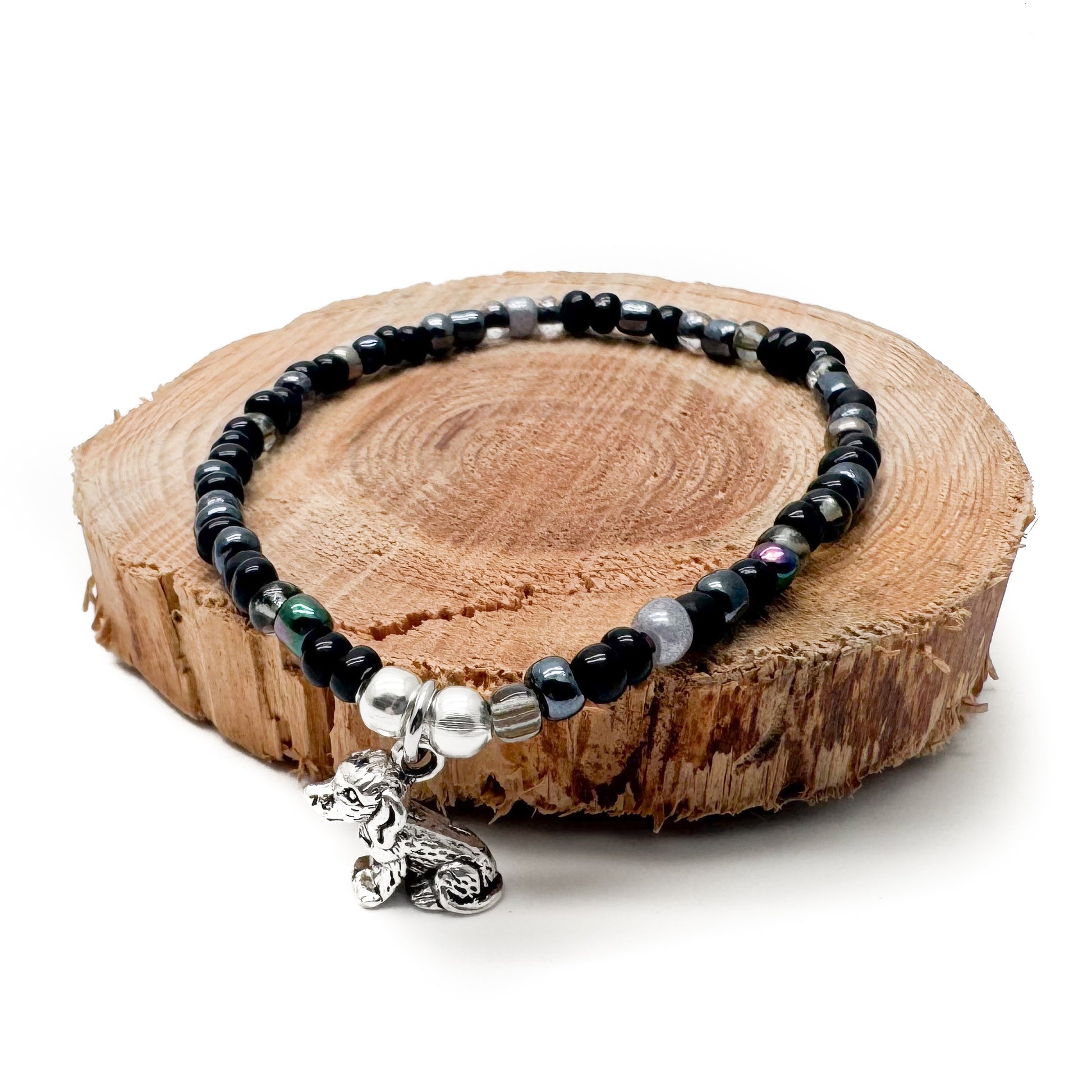 A bracelet made of black beads and silver beads is displayed on a wooden log.