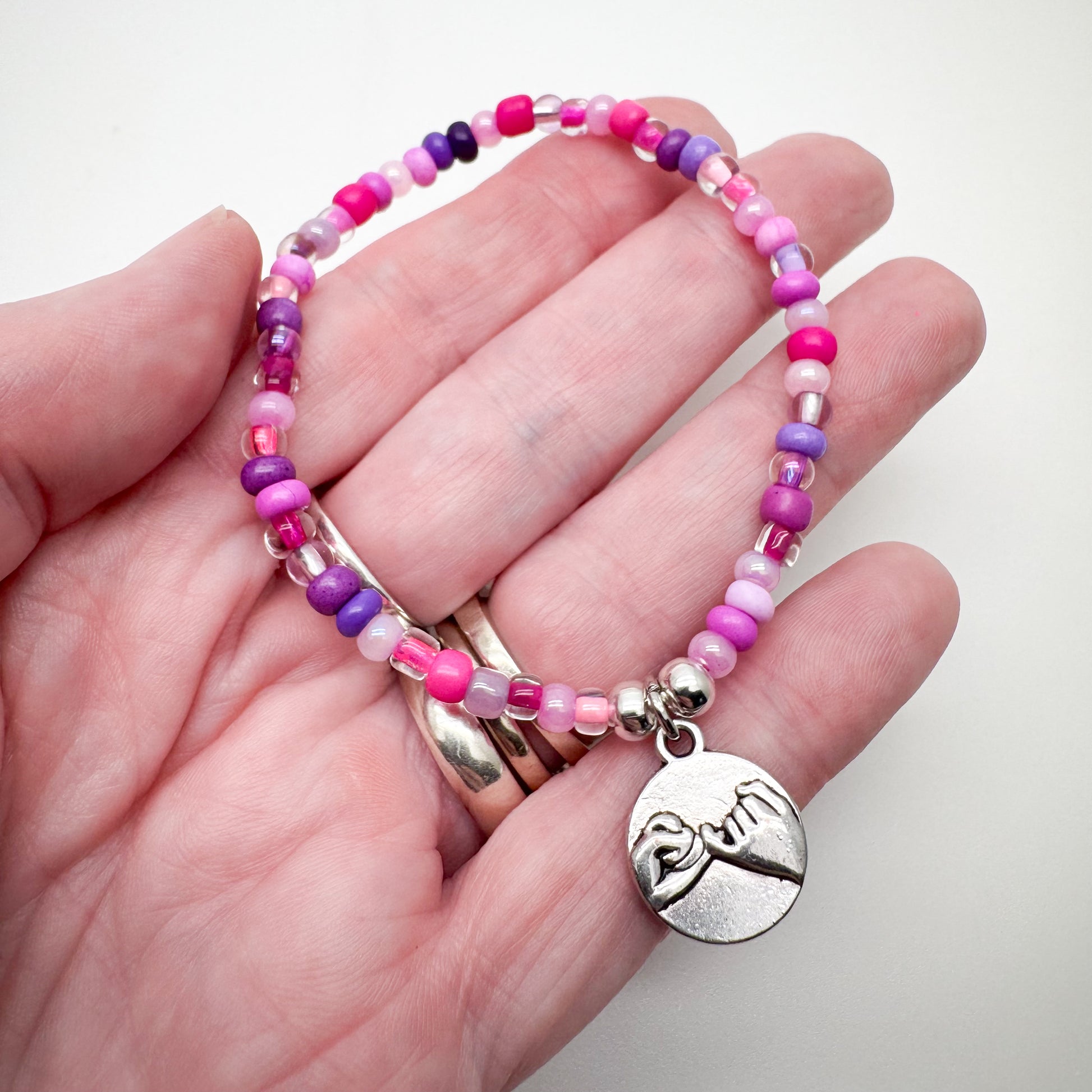 A hand holding a bracelet made of colorful beads and a charm with a hand gesture on it.