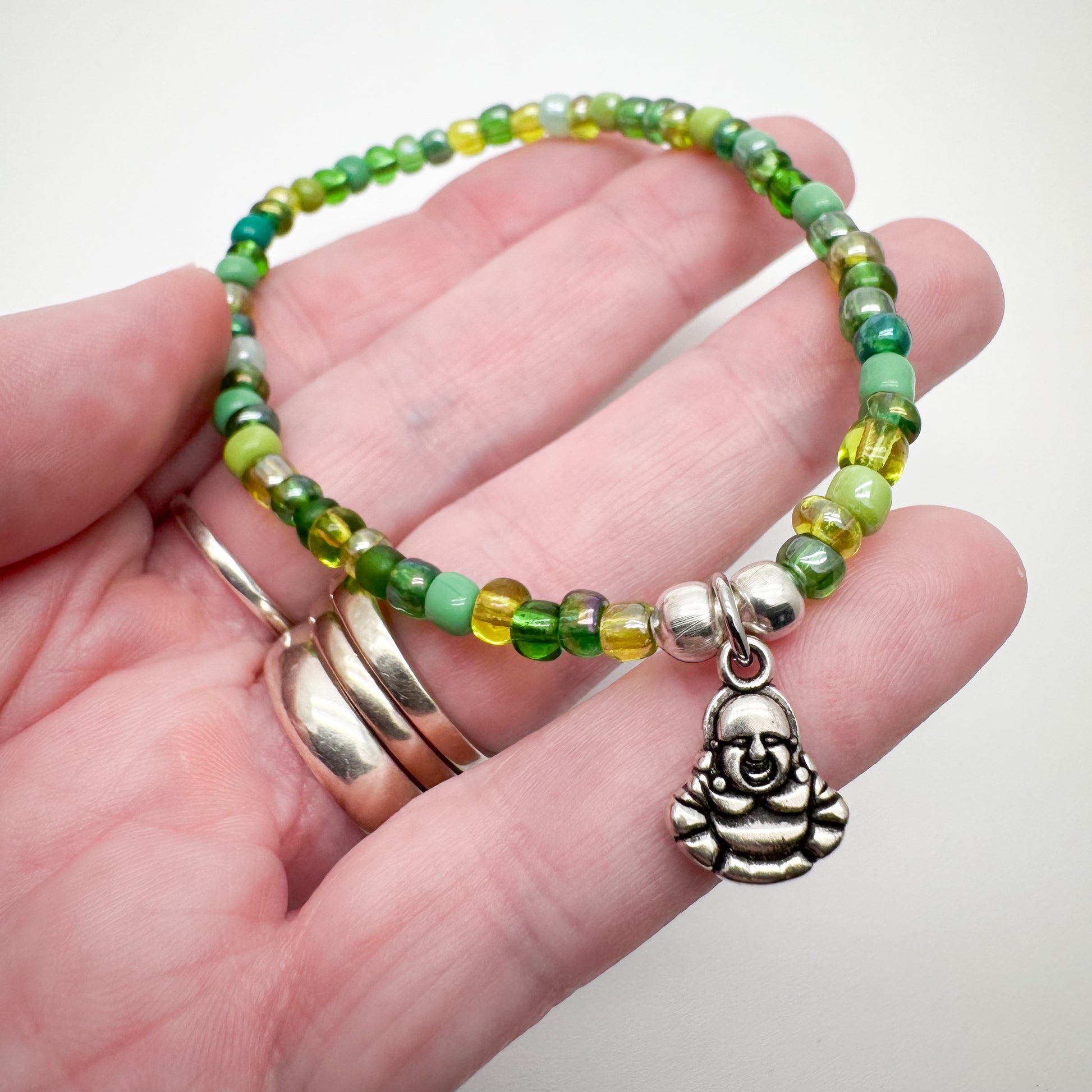 A hand holding a bracelet made of green beads and a charm featuring Buddha imagery.