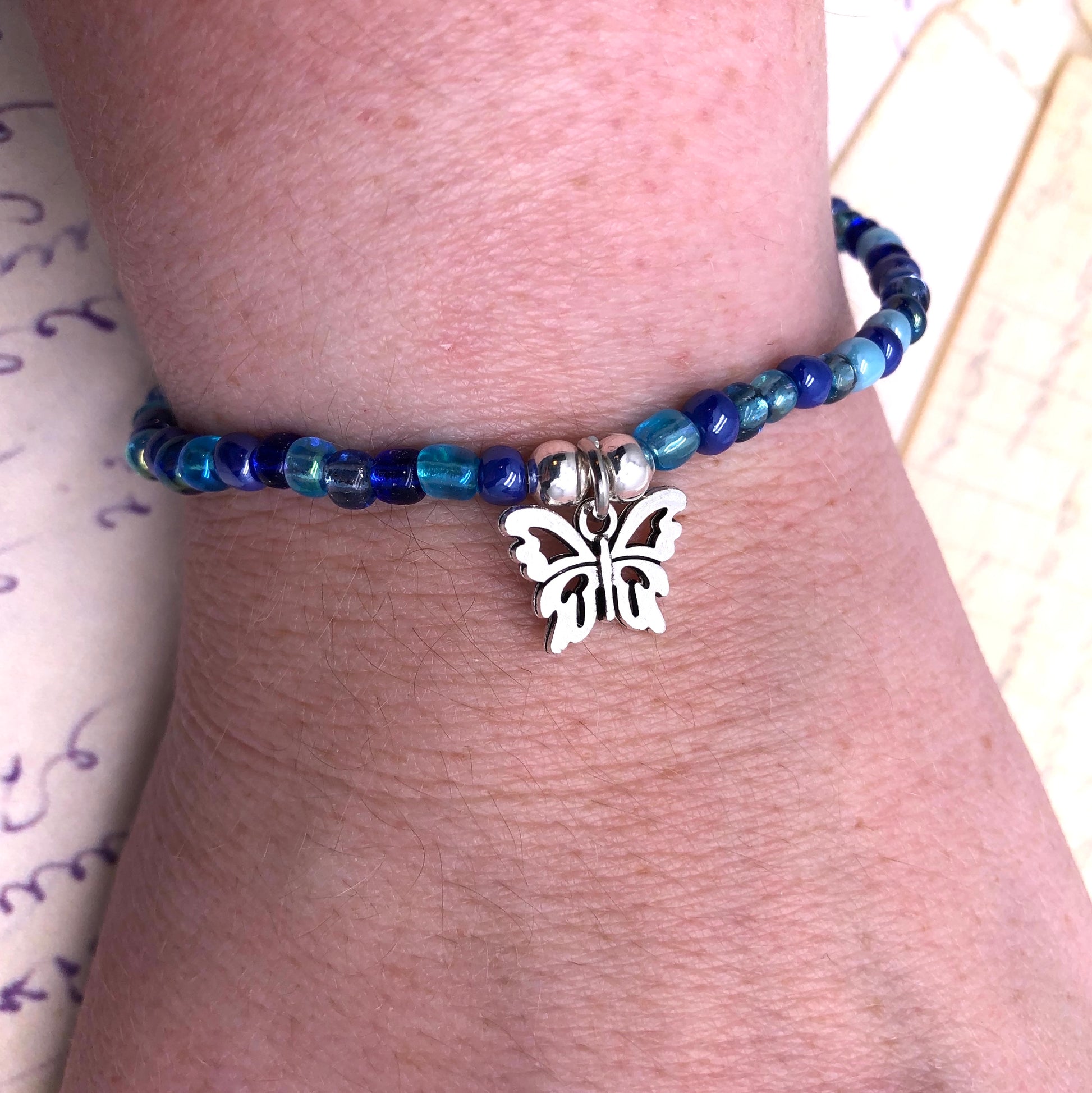 A bracelet with blue beads and a silver butterfly charm on a person's wrist.