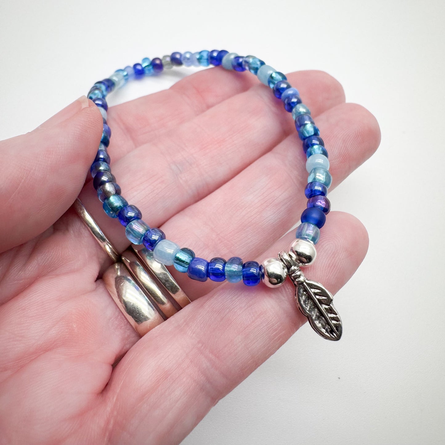 A hand holding a bracelet made of blue and silver beads, with a silver leaf charm attached.