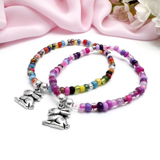 two beaded bracelets with charms, placed on a pink fabric background.