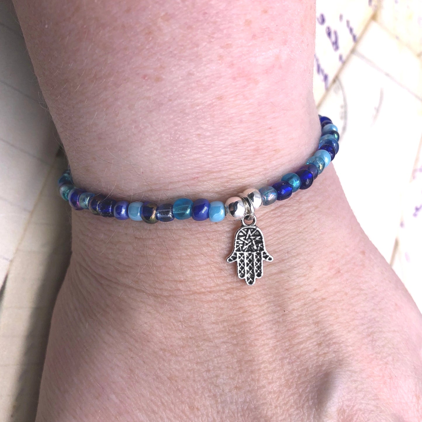 A bracelet made of blue beads and a silver Hamsa charm is worn on a person's wrist.