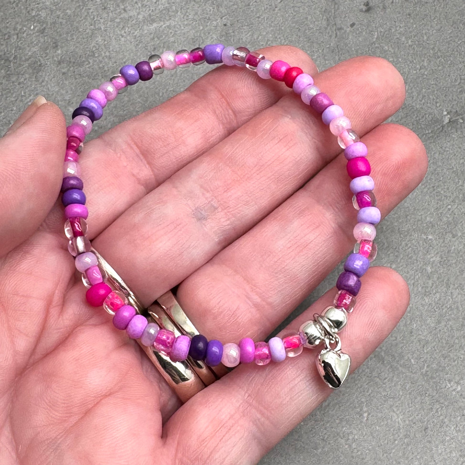 A hand holding a bracelet made of colorful beads, including shades of pink, purple, and clear beads.