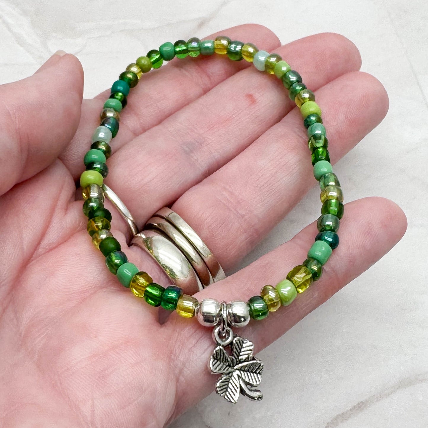 A hand holding a bracelet made of green beads and a charm featuring a four-leaf clover.