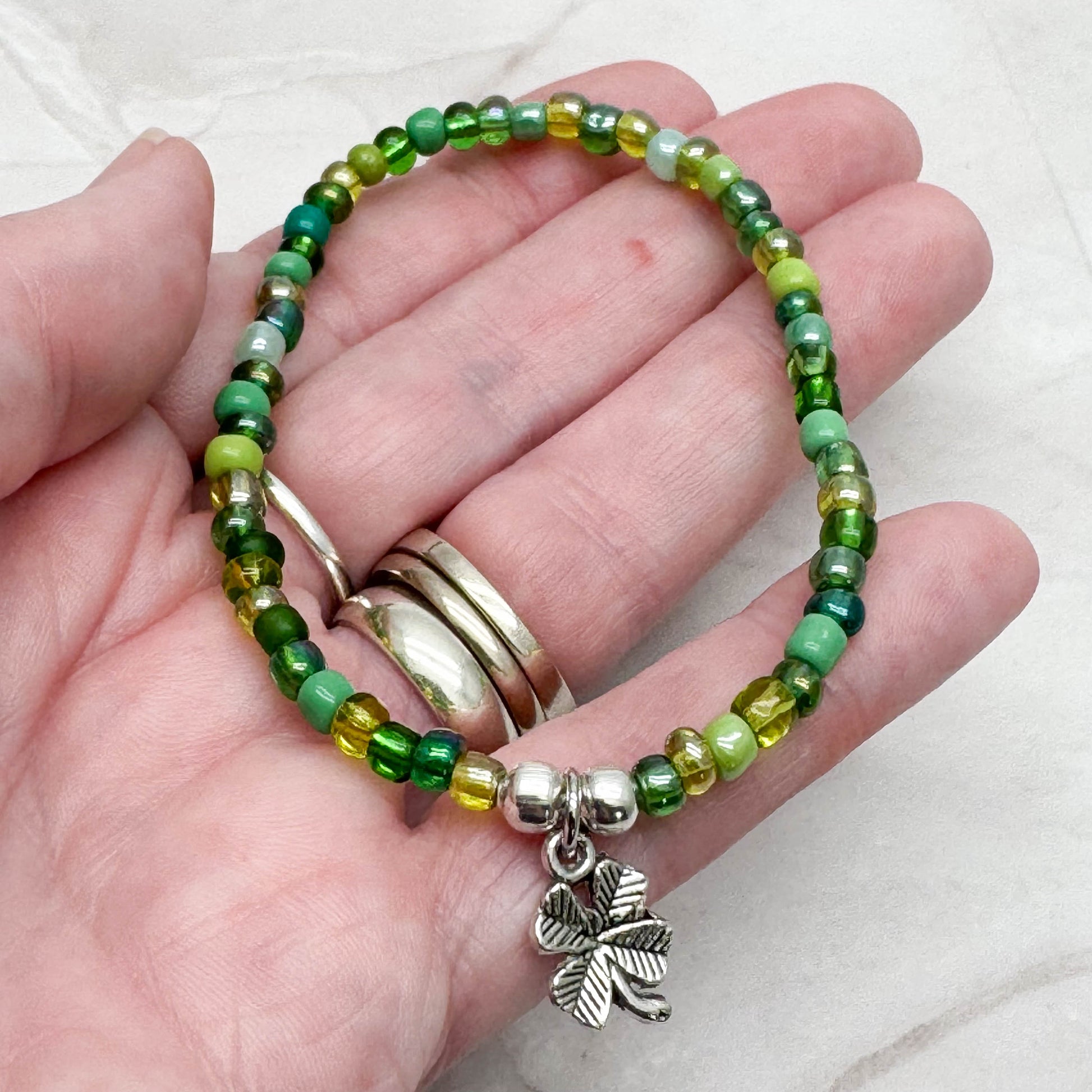 A hand holding a bracelet made of green beads and a charm featuring a four-leaf clover.