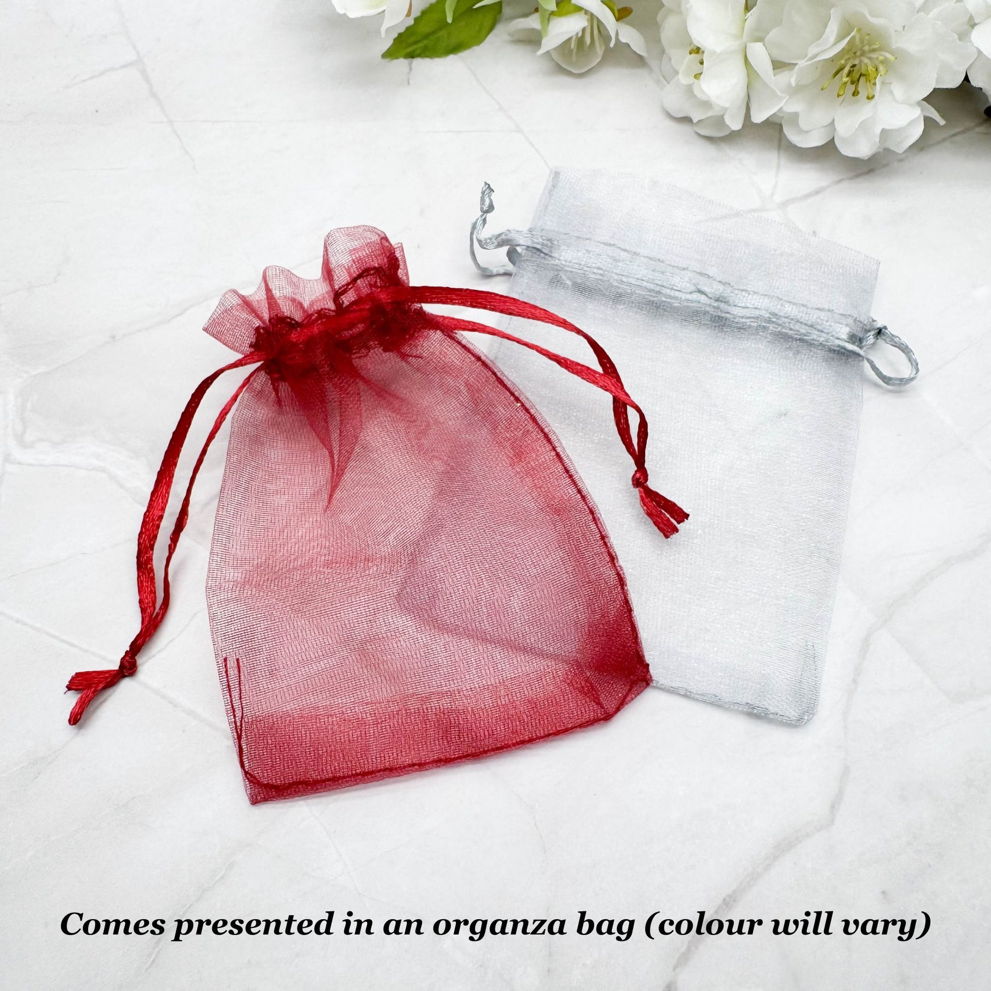 A red and white gift bag with a red ribbon, placed on a white marble surface, with white flowers in the background.