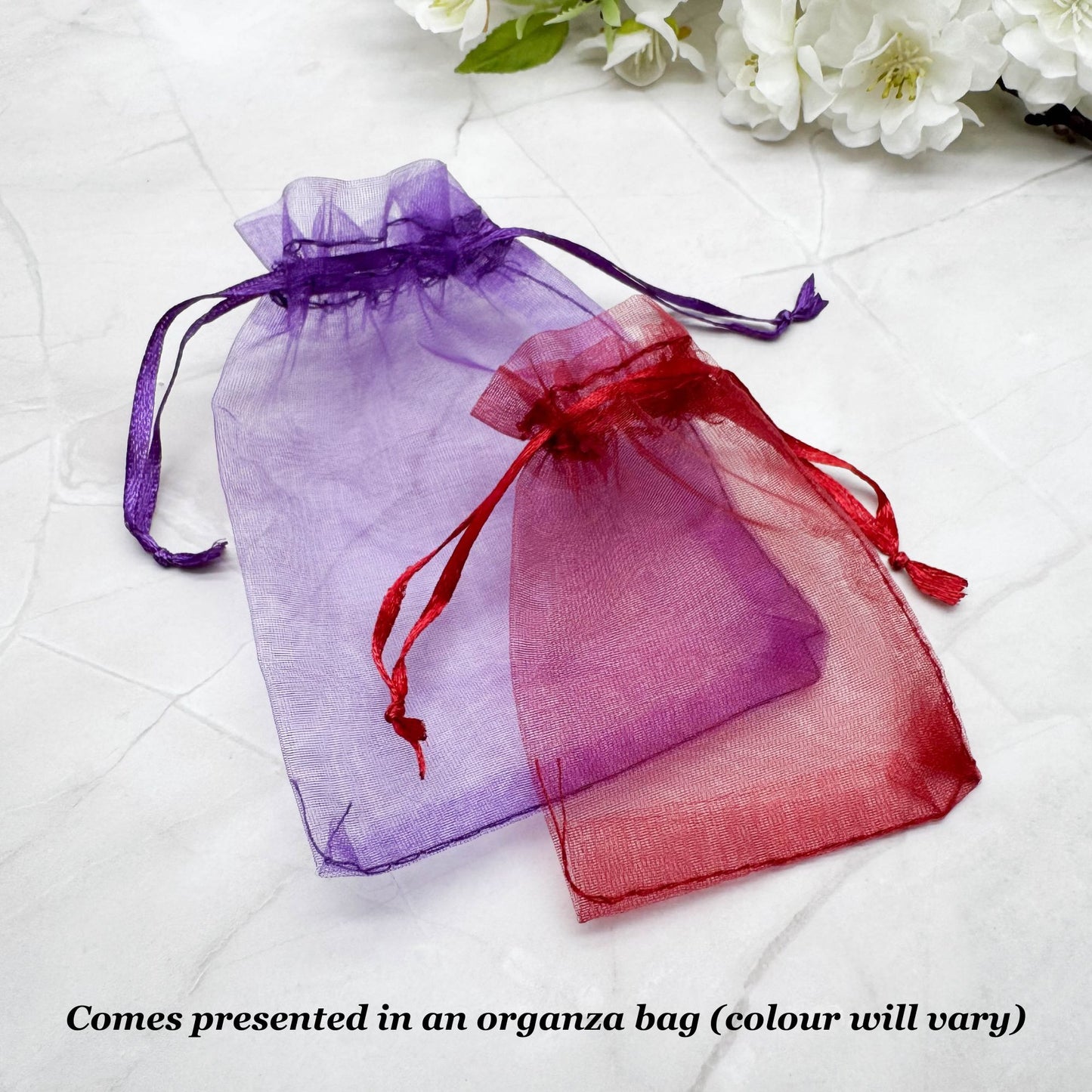 two transparent fabric bags, one purple and one red, tied with red ribbons, placed on a white surface.